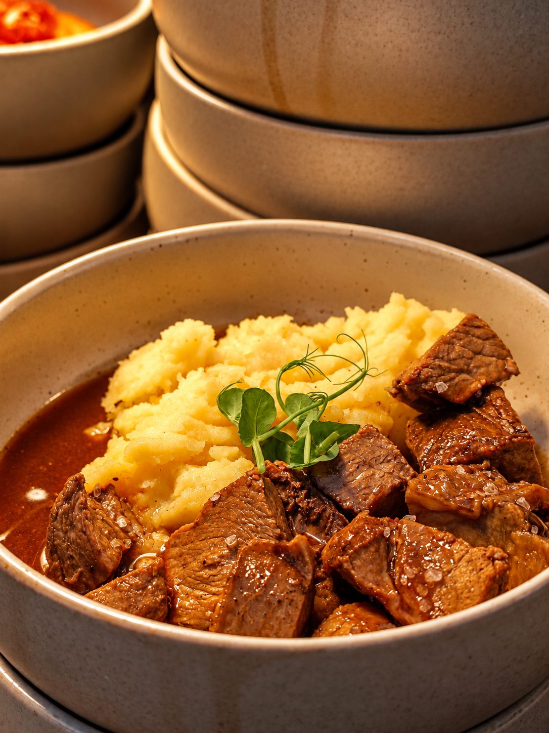 Bowl of braised beef with creamy mashed potato and a pea shoot