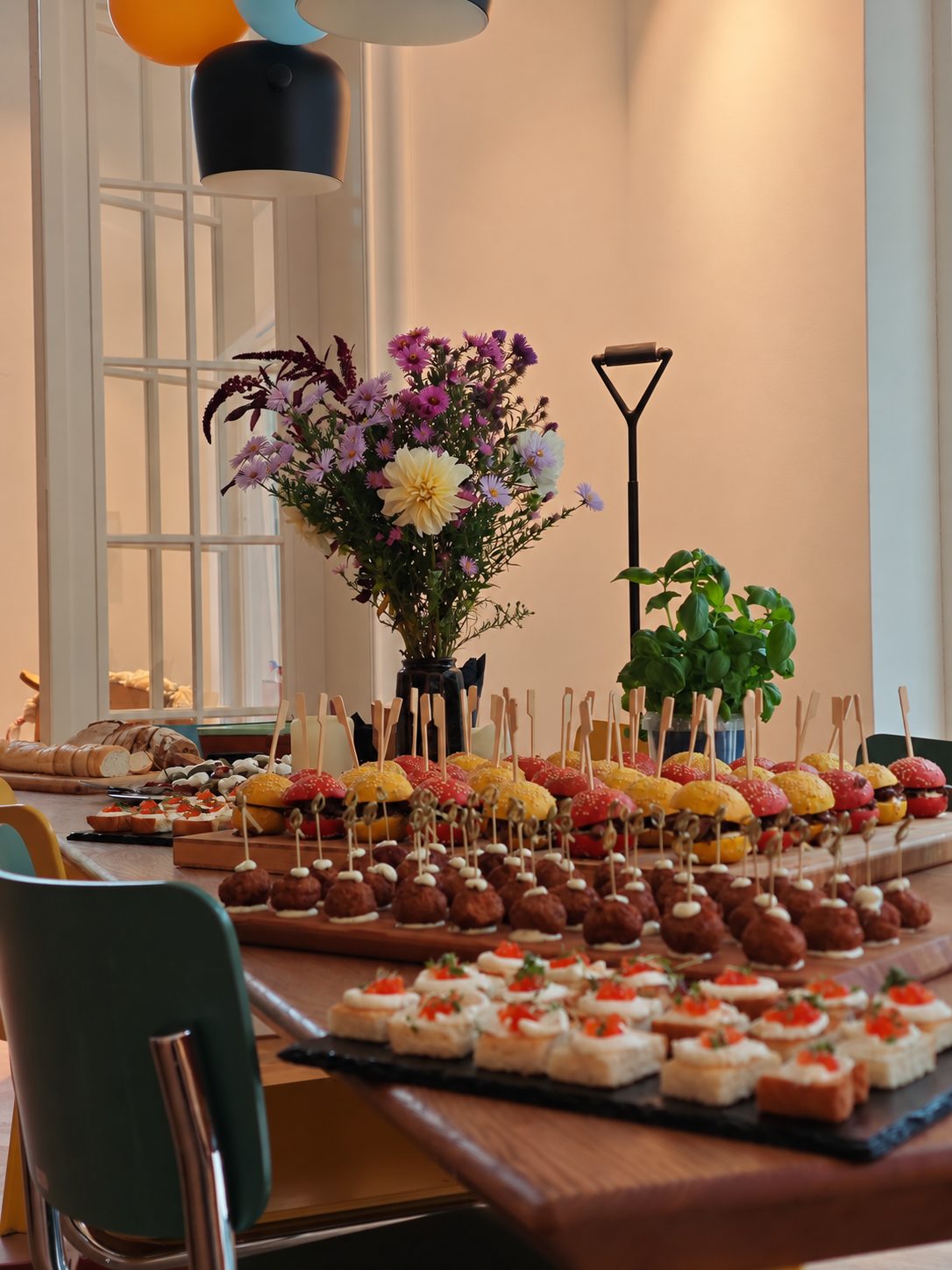 Table with canapés, mini burgers and meatballs next to a wildflower bouquet
