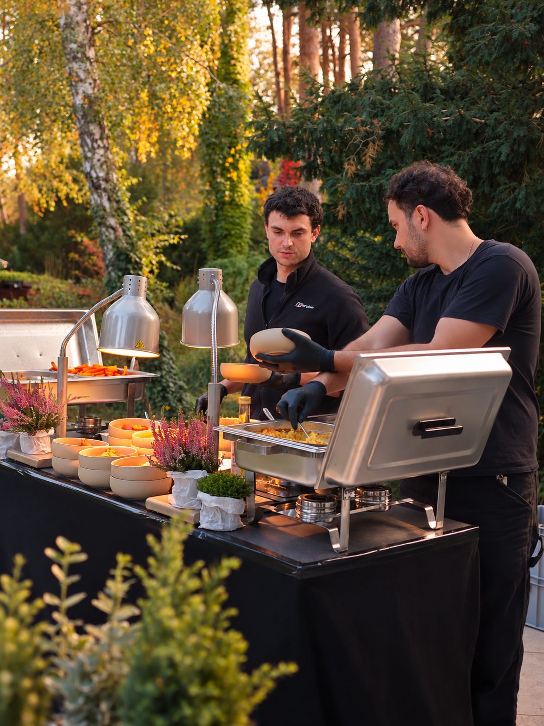 Buffet in a garden at golden hour, two chefs serving from chafing dishes