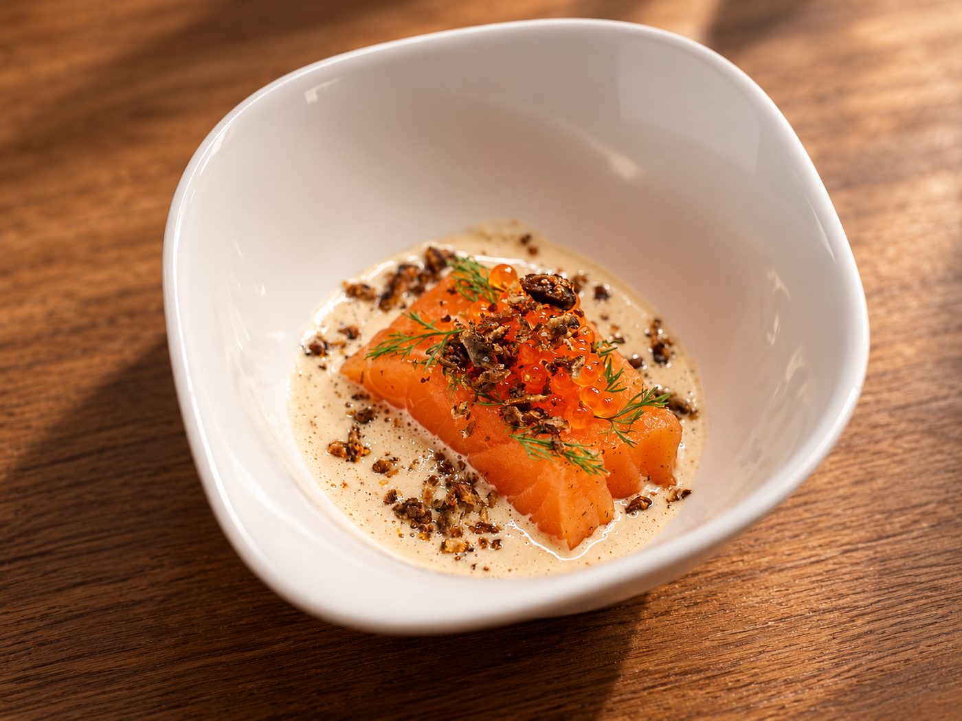 Salmon fillet with ikura, dill and a crispy topping in a creamy sauce in a white bowl