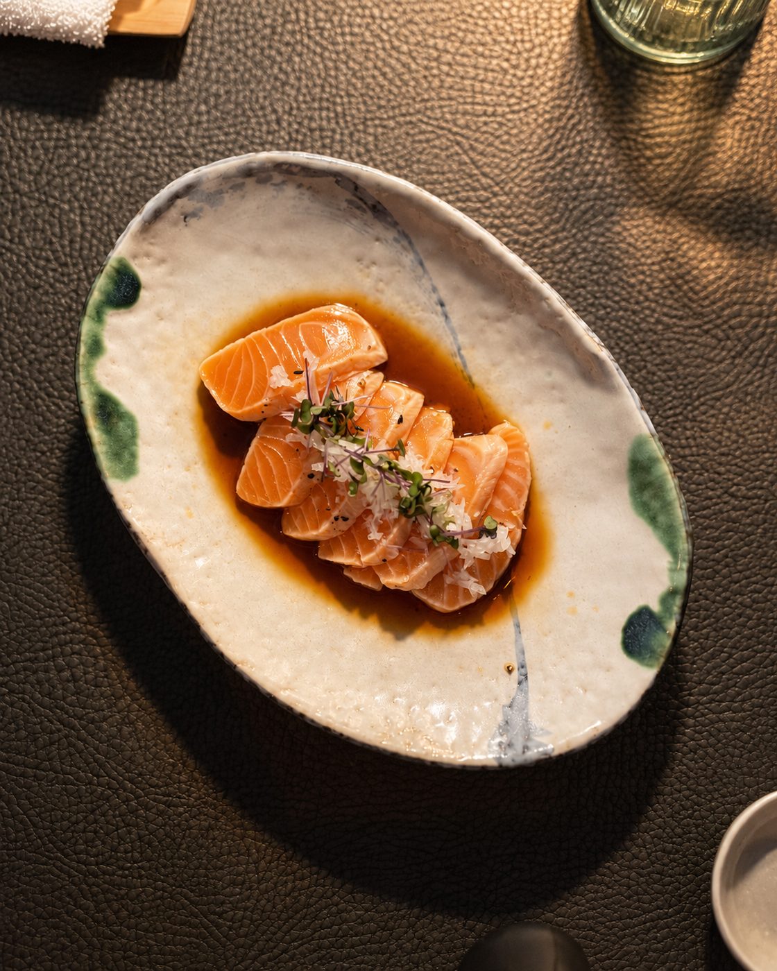 Salmon sashimi in soy sauce with micro herbs on a ceramic plate